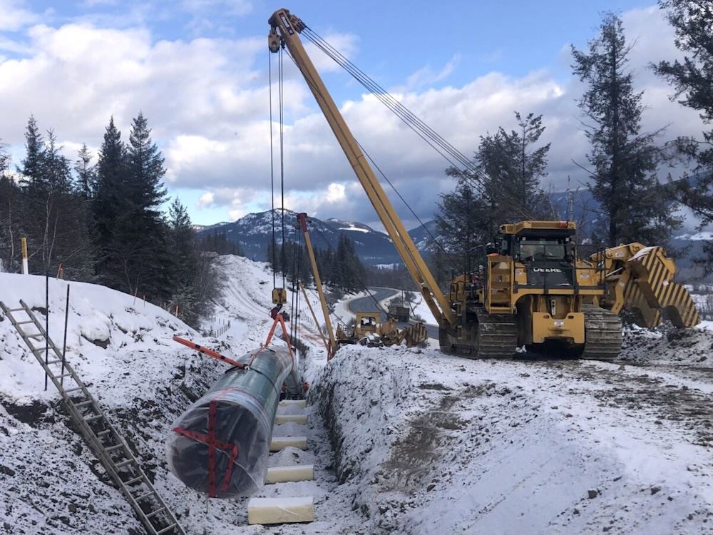 A pipeline is lowered into a trench. There is a thin layer of snow on the ground.