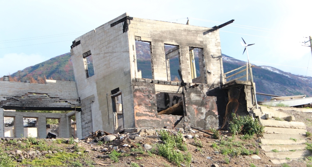 A burned-out building in front of a rugged mountain.
