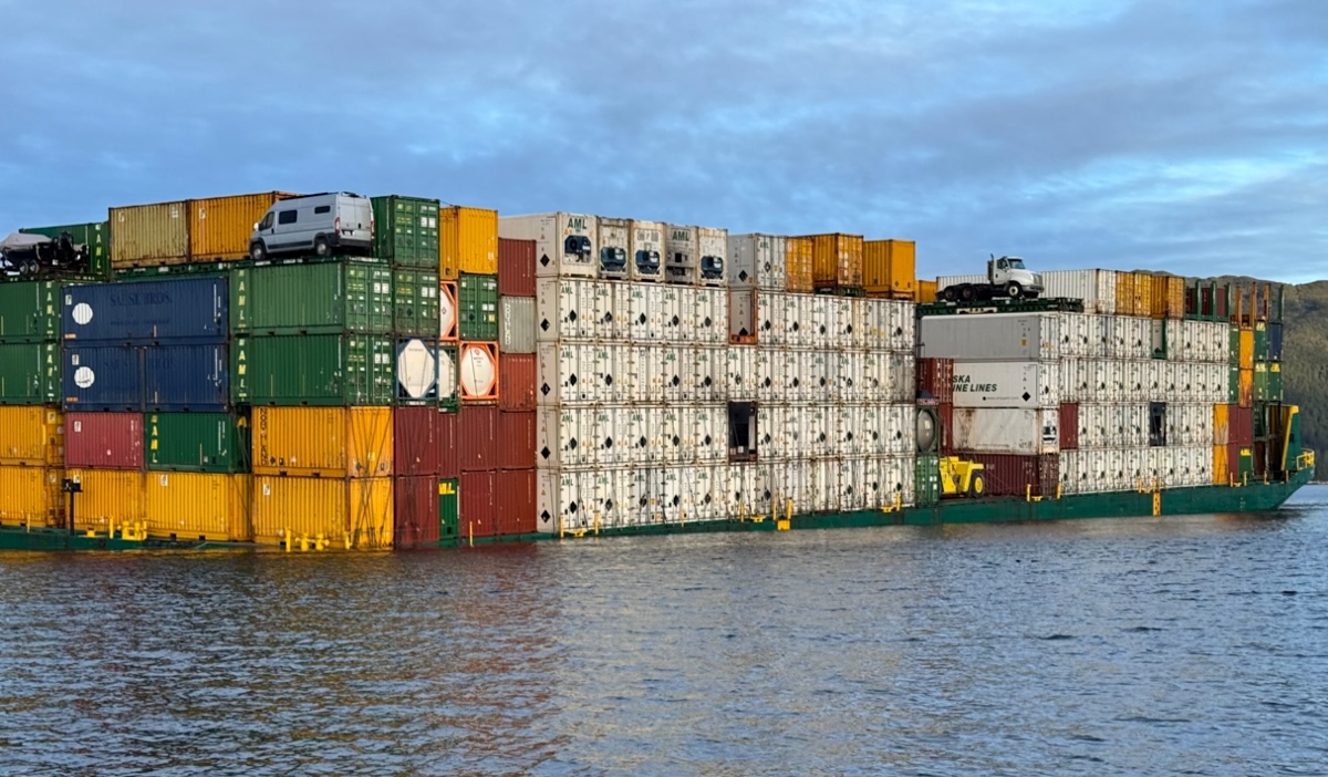 A very large barge with containers of various colours is partially submerged, with its deck sitting nearly at water level.