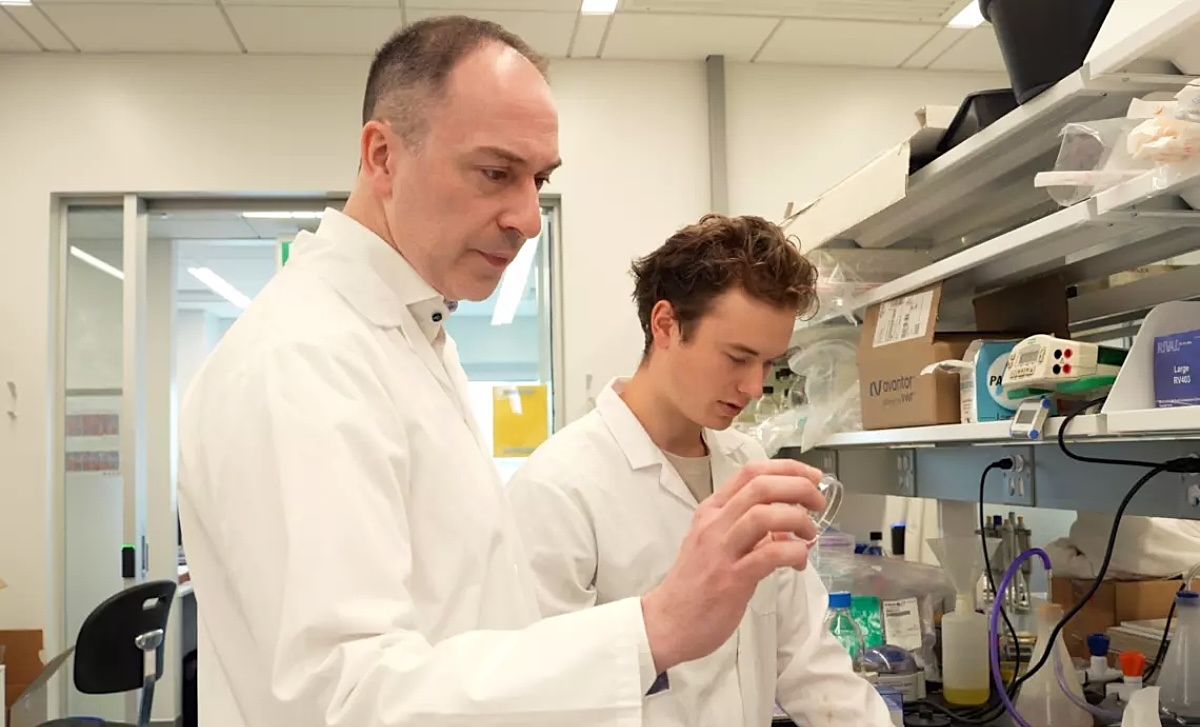 Two light-skinned scientists wearing lab coats examine specimens.