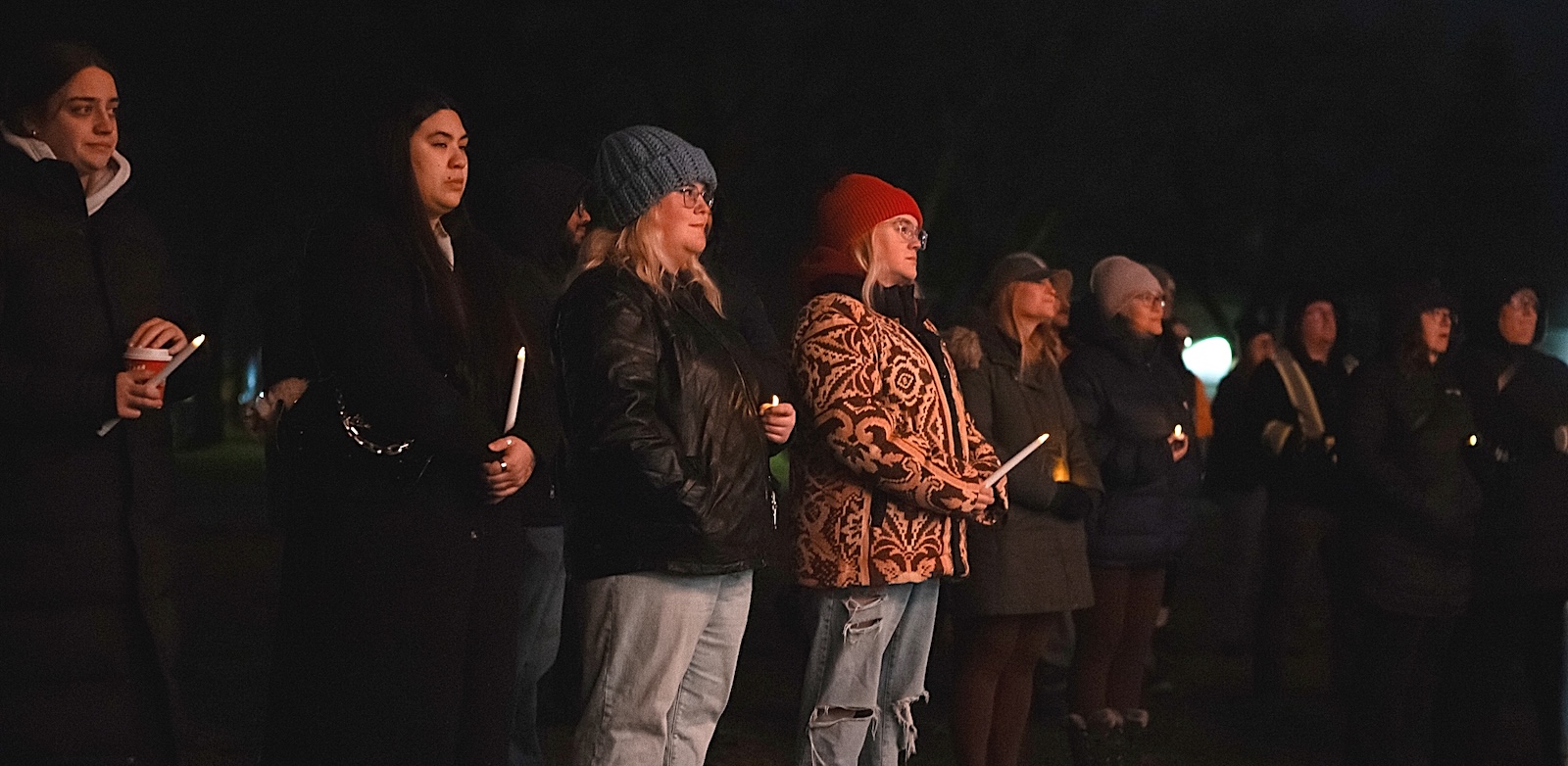 Sombre men and women in winter garments stand listening to those speaking.