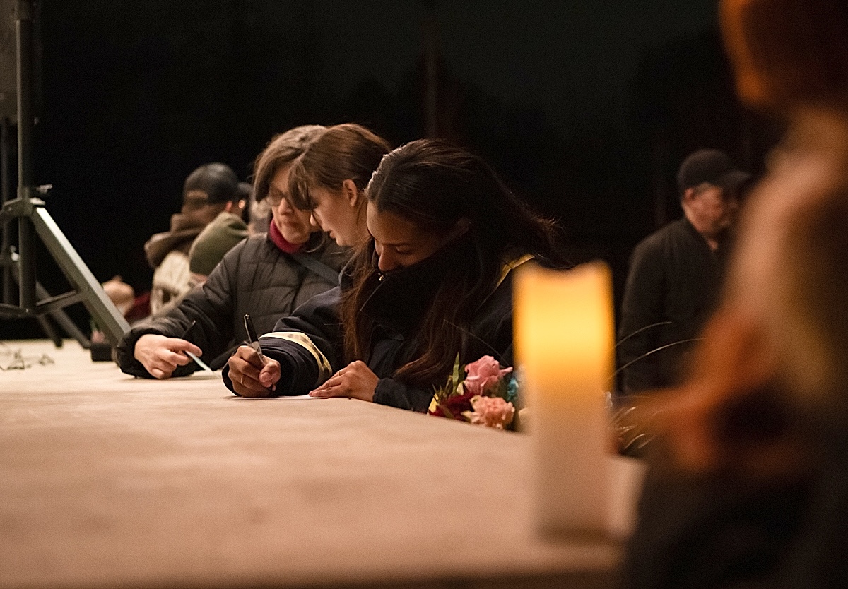 A woman in winter gear uses a flat platform to write a message on a card.