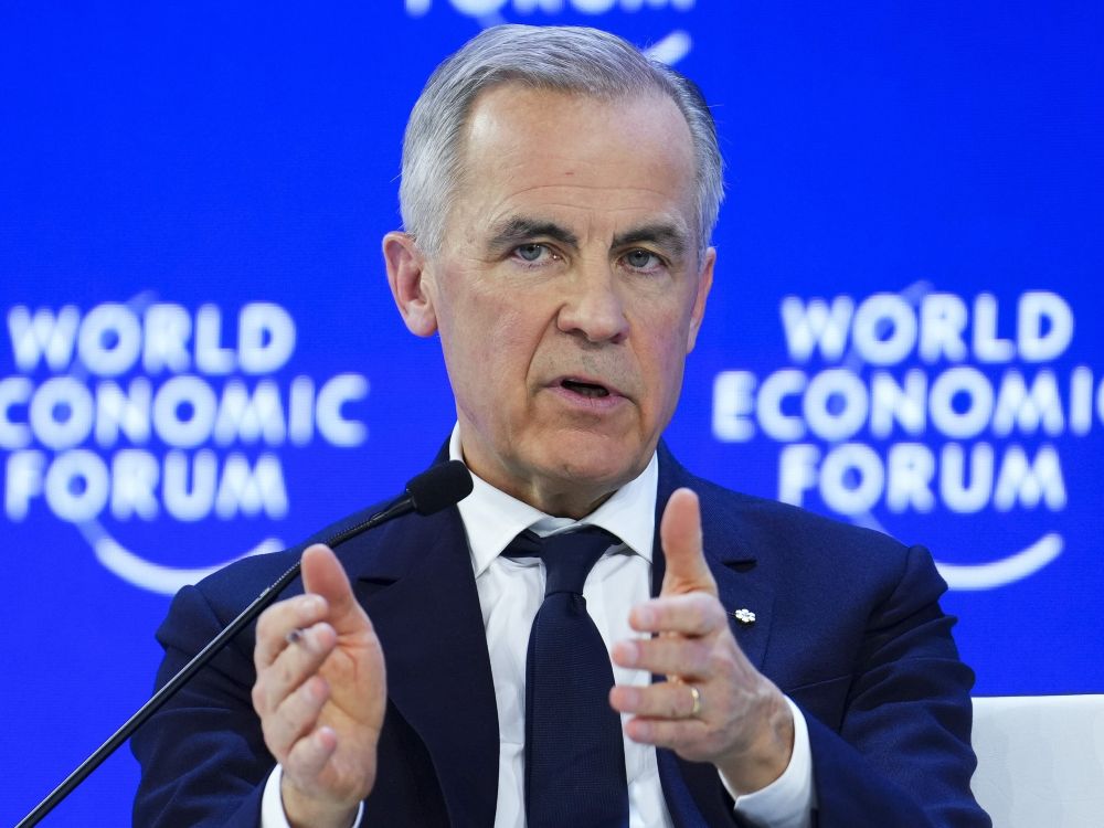Mark Carney, a 60-year-old light-skinned man gestures as he speaks at podium, with a blue background that says &ldquo;World Economic Forum.&rdquo; 