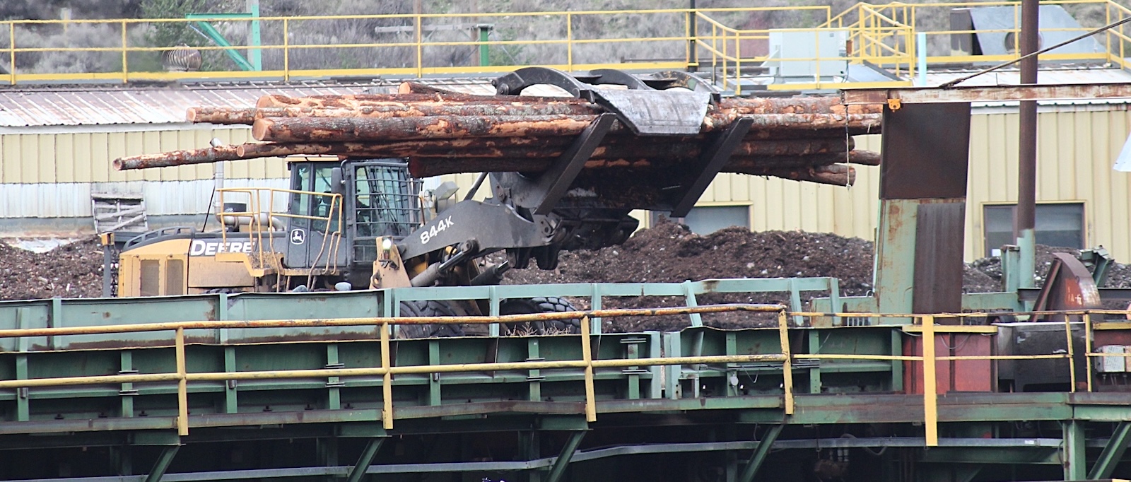 A yellow loader transports logs at a lumber mill. 