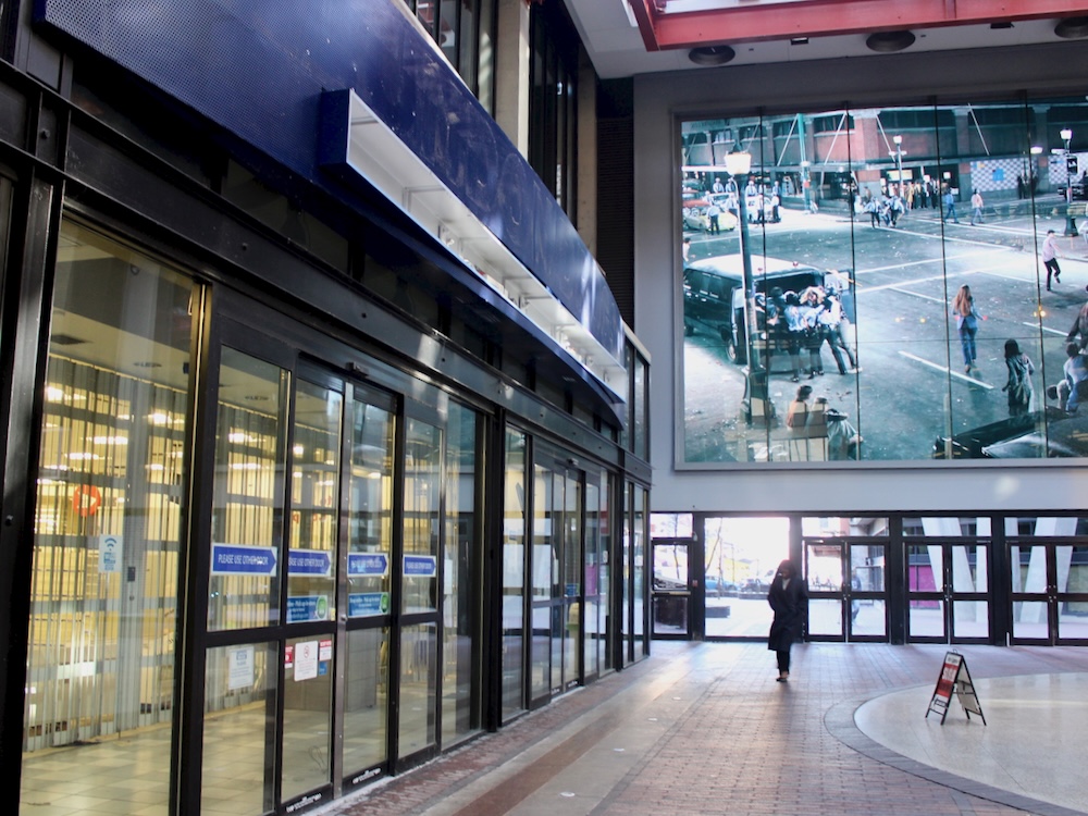 An empty storefront in the indoor atrium at Woodward&rsquo;s in downtown Vancouver. A blue awning over the sliding doors shows an empty space where the London Drugs sign used to be.