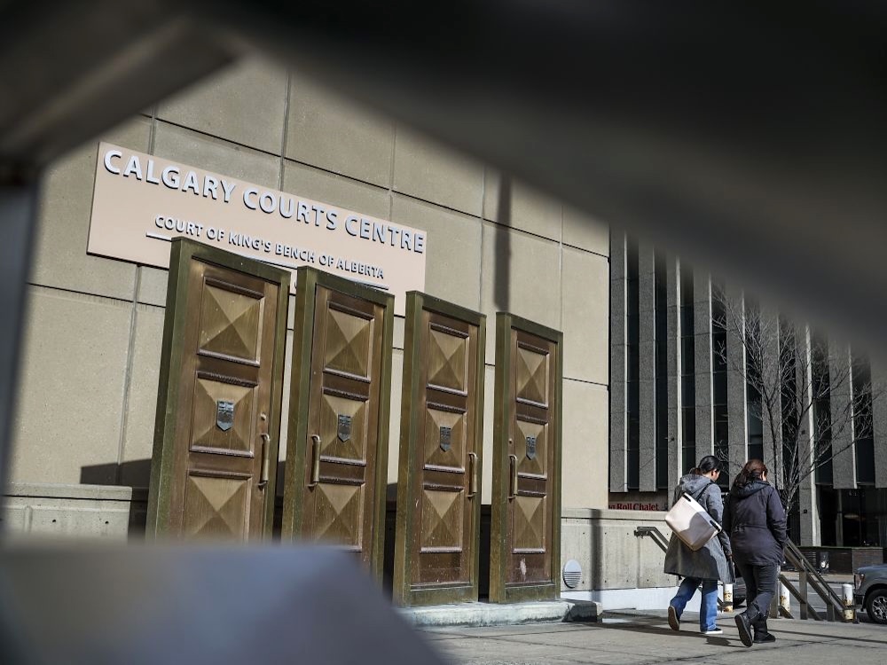 The outside of a building with the sign &lsquo;Calgary Courts Centre&rsquo; and two people walking by on a sunny day.