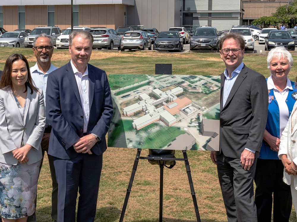 Adrian Dix and several other people stand on what was announced as the future site of the Beedie Long-Term Care Centre in Delta. There is a placard showing a rendering of what the centre will look like.