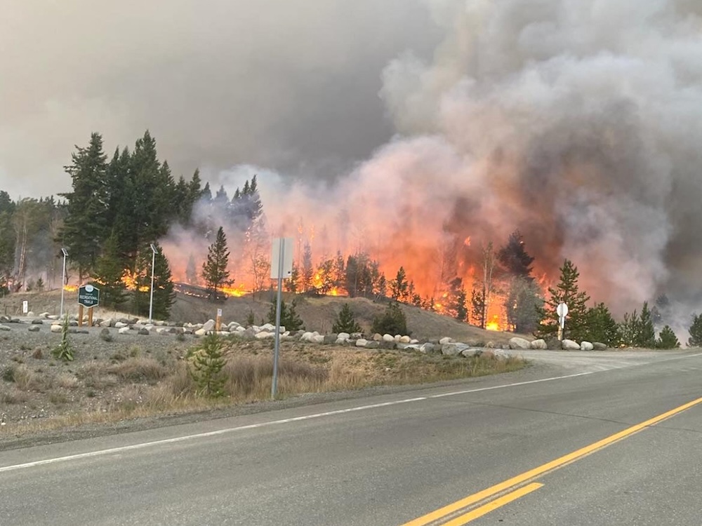 Flames are seen in the distance outside a community in a dry, semi-arid landscape.