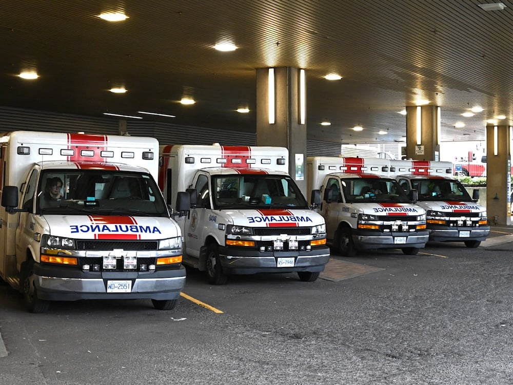 Four ambulances are parked on a diagonal in an ambulance bay lit by many pot lights.