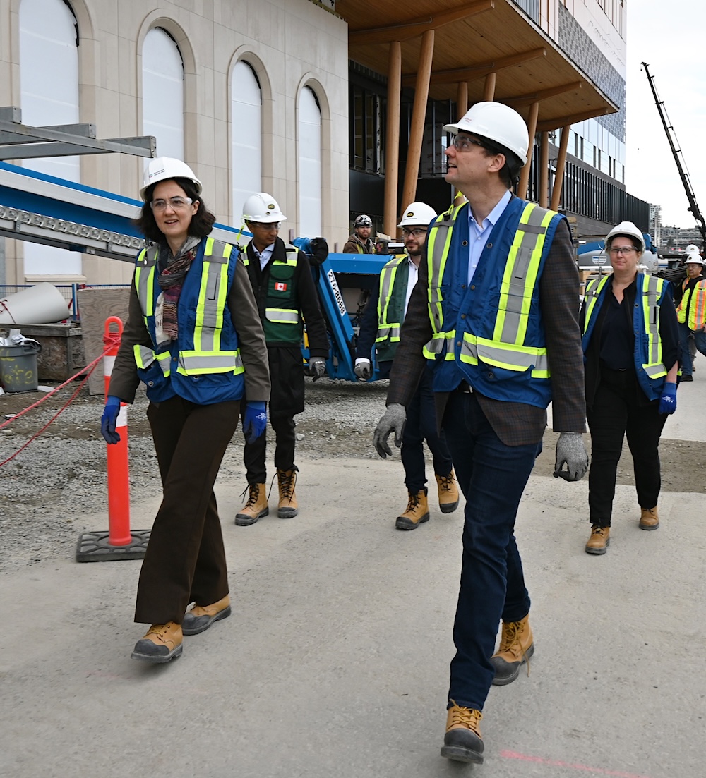 Premier David Eby wears a blue high-visibility vest, a white hard hat and brown steel-toed boots as he walks in front of the new St. Paul&rsquo;s Hospital.