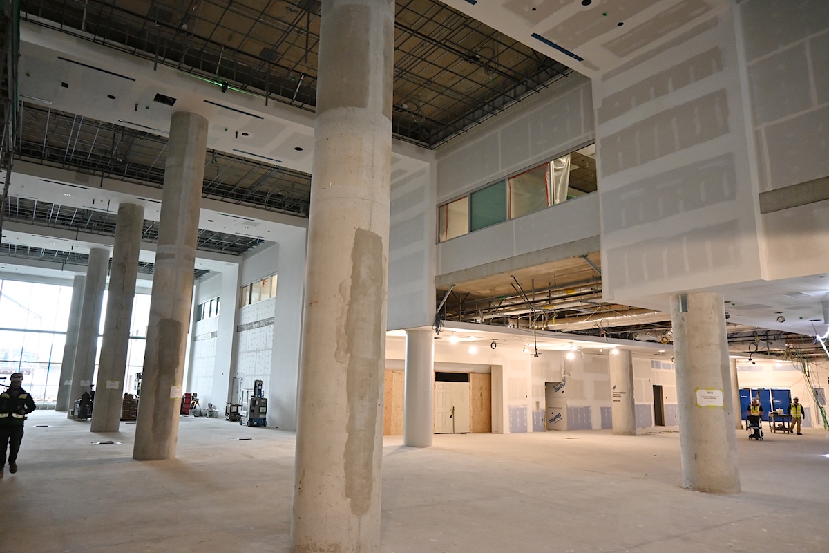 A large, unfinished room with concrete floors, pillars and walls is brightly lit by windows. The ceiling is unfinished and the rebar built into the structure is visible.