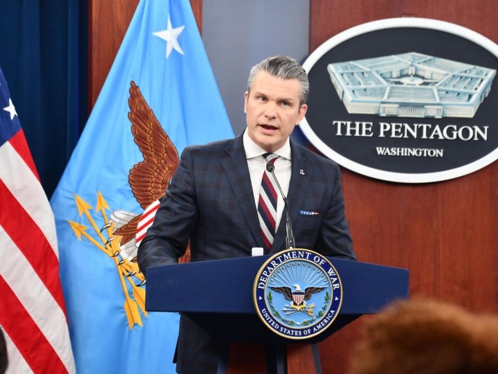 Pete Hegseth, a 45-year-old light-skinned man with slicked back greying hair, stands at a podium in the Pentagon.