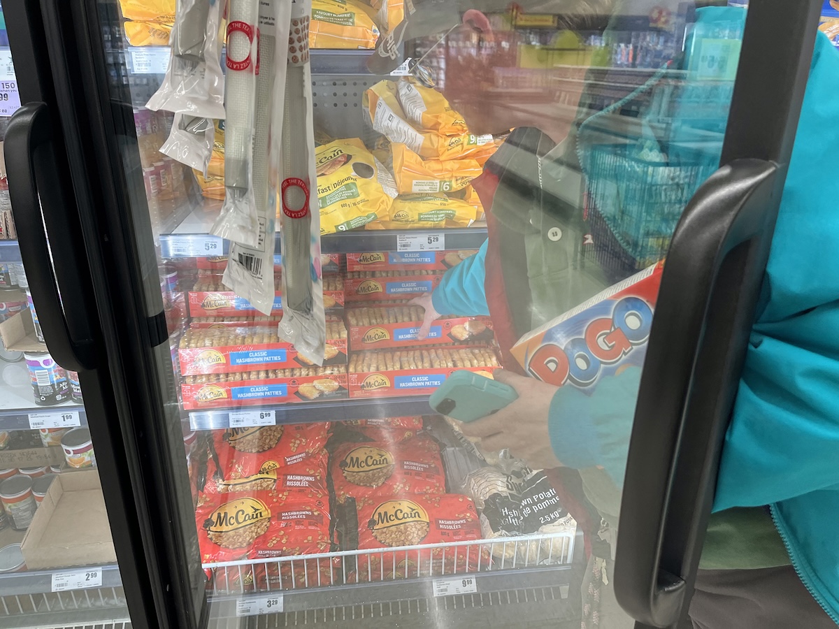 A man with light skin tone chooses a pack of hash browns from the frozen section at the grocery store.