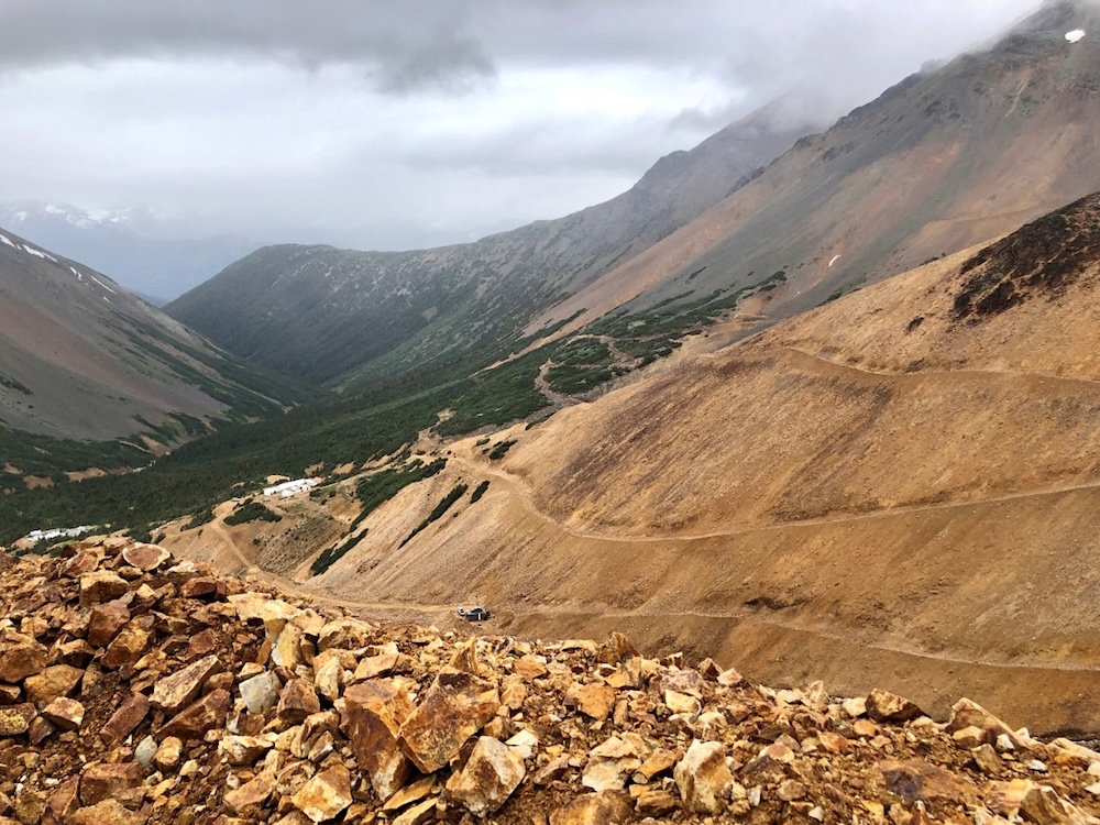 A ridge of orange-hued rocks sits in the foreground, in front of an orange, rocky mountainside with mining roads.