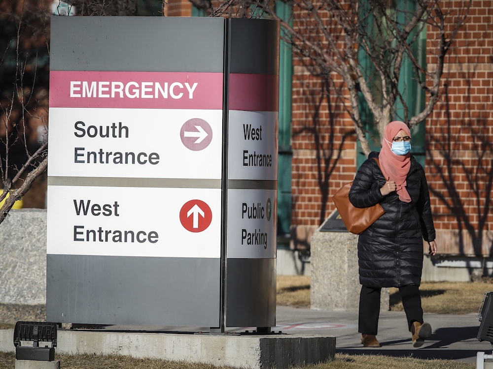 A person walks past a hospital, with a large sign directing people to different entrances.