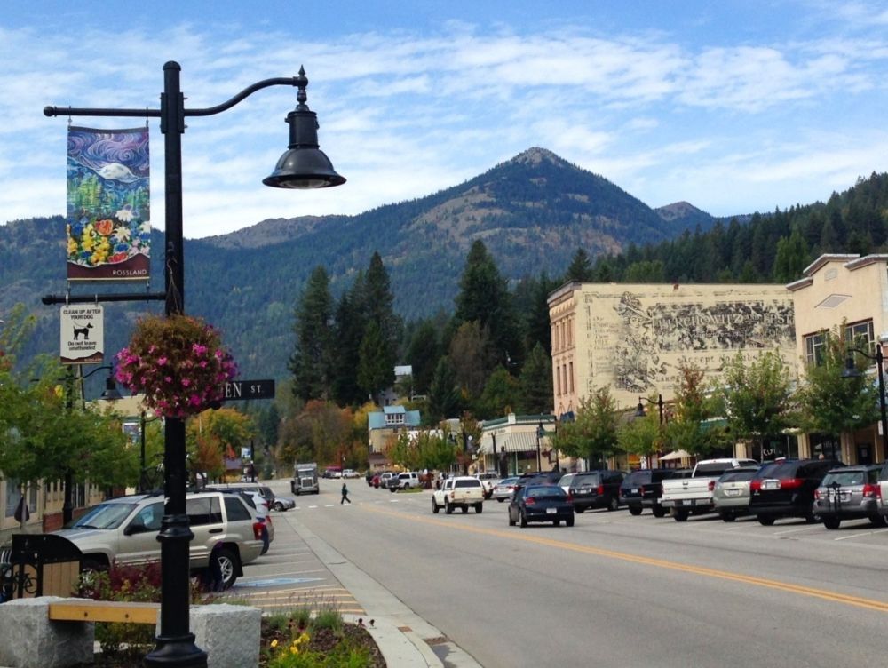 A cast iron standard and street lamp in the style of the late 1800s partially frames a small town&rsquo;s storefront-lined main street with a mountain rising in the background.