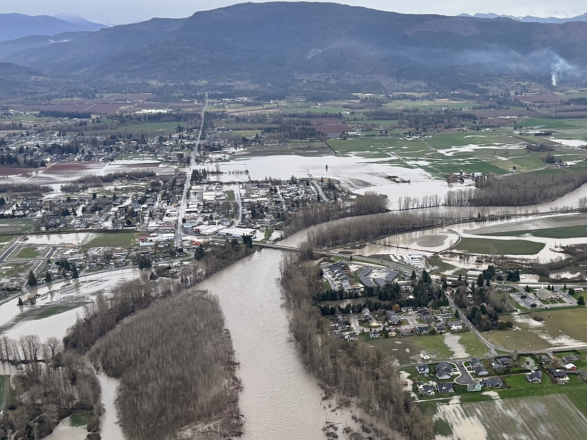 An aerial photograph shows a bridge across a muddy river, with flooding visible in the surrounding community.