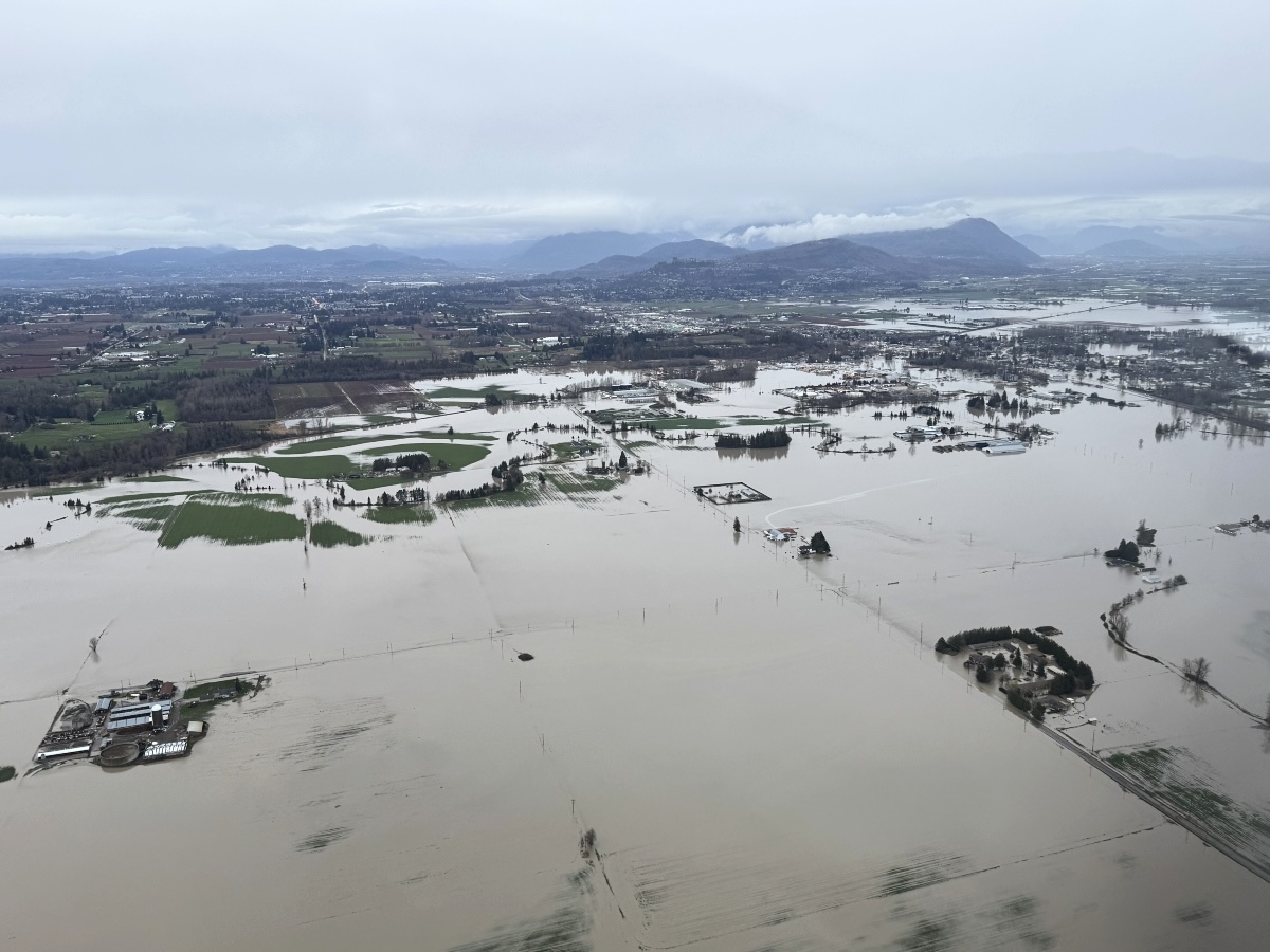 An aerial photograph shows farmland inundated by water, which continues into the horizon towards distant hills.