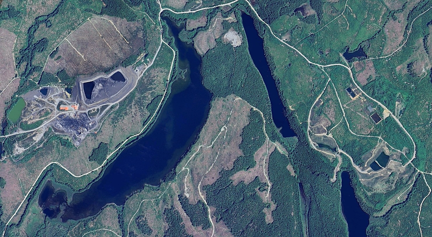 A satellite image showing a small mine site with a few buildings near a U-shaped lake and, on the other side of that lake, a long, narrow lake.