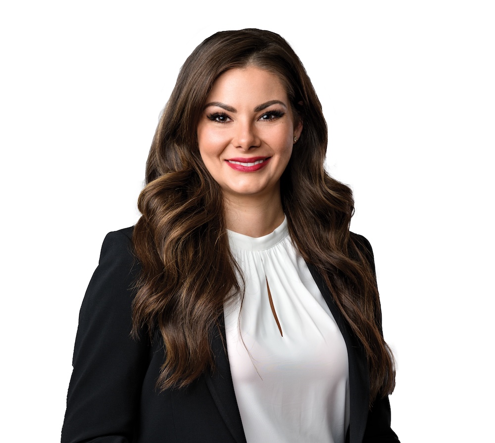 A woman with light skin tone and long, dark, wavy hair wears a suit.
