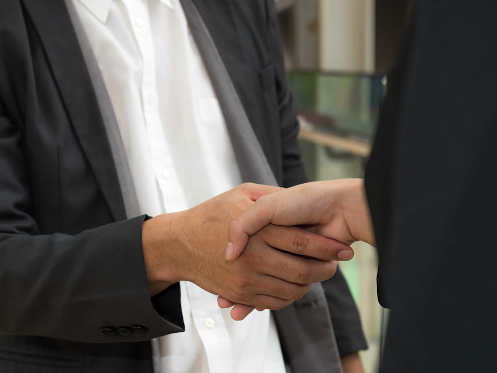 A close-up of the torsos of two people in suits shaking hands.