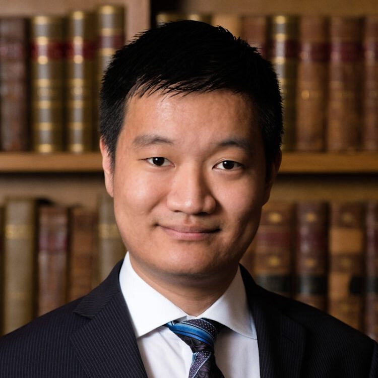 A man with medium-light skin tone and short, straight dark hair wears a suit.
