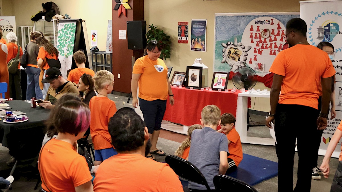 Adults and children in a classroom, most of whom are wearing bright orange T-shirts.