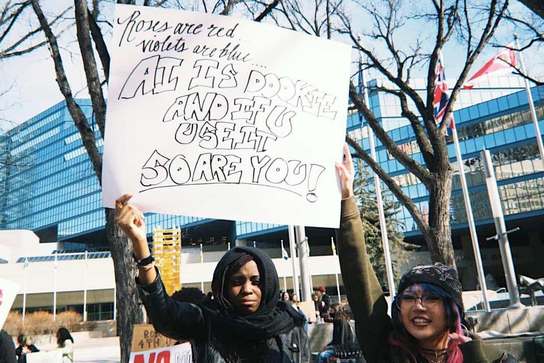 Two young people hold a sign that says &lsquo;AI is dookie and if you use it so are you.&rsquo;