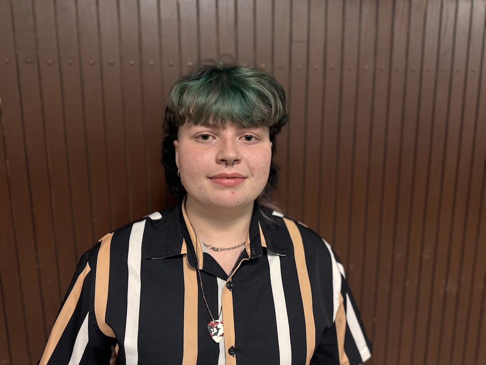 A teenager with green hair and a striped shirt.