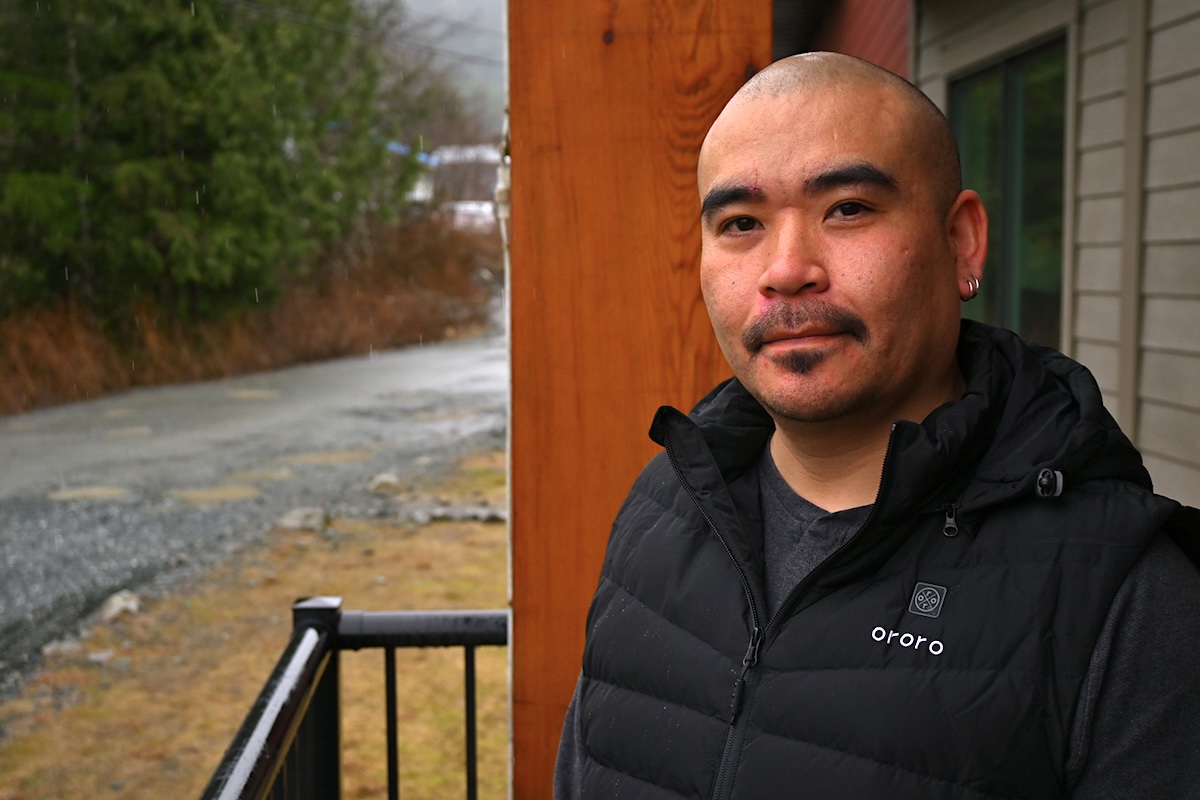 An Indigenous man with a shaved head, moustache and medium skin tone looks directly at the camera.