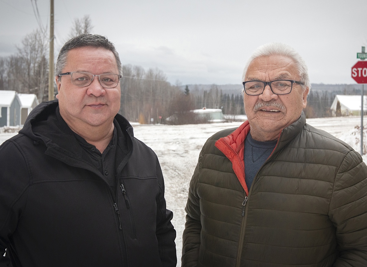 Two men wearing glasses and winter coats stand outdoors in a snowy setting.