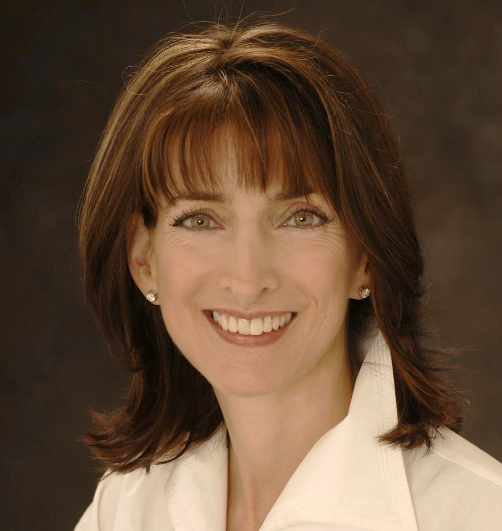 Headshot of a woman with light skin and shoulder-length brown hair and bangs.