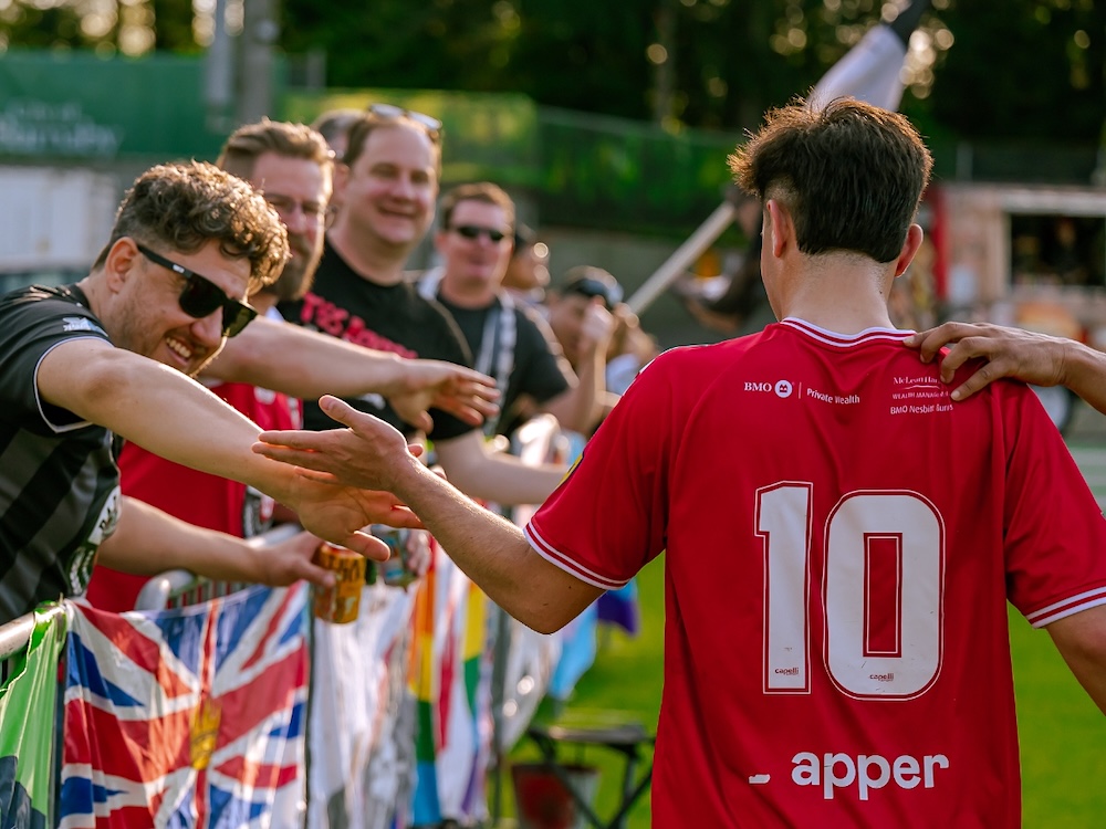 Fans of a soccer team stand behind a short fence and high-five a passing player.