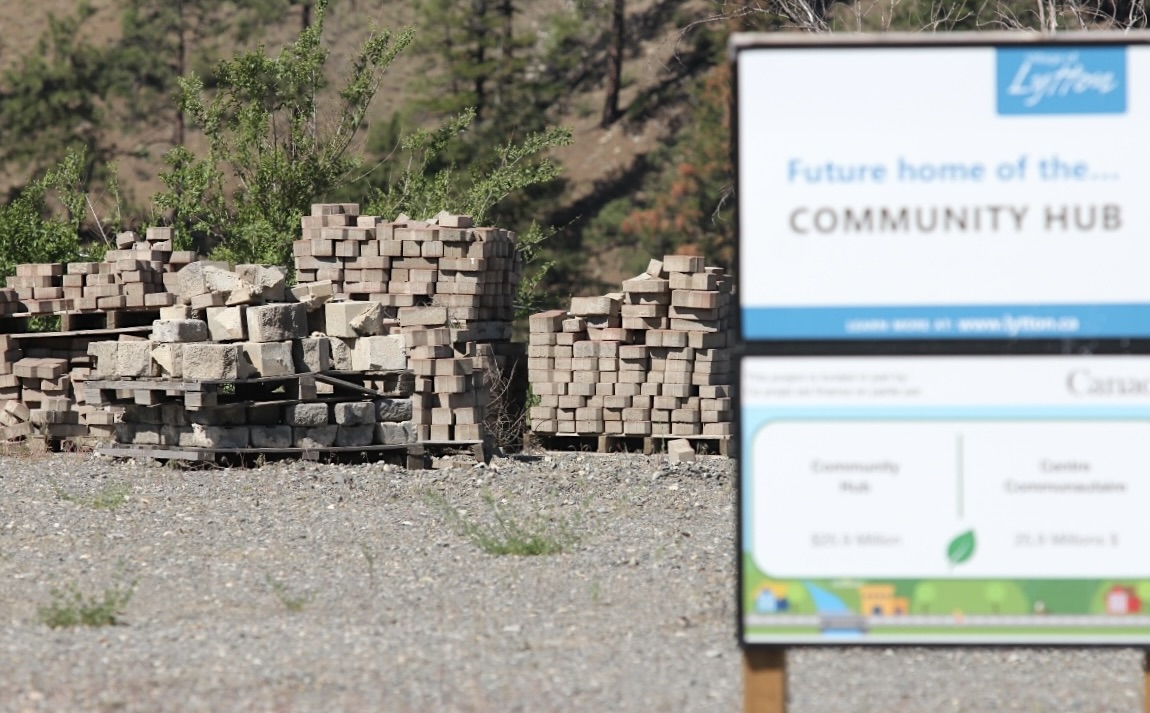 A pile of bricks sits on a gravel lot. In the foreground, a blurred sign says, &lsquo;Community Hub.&rsquo;