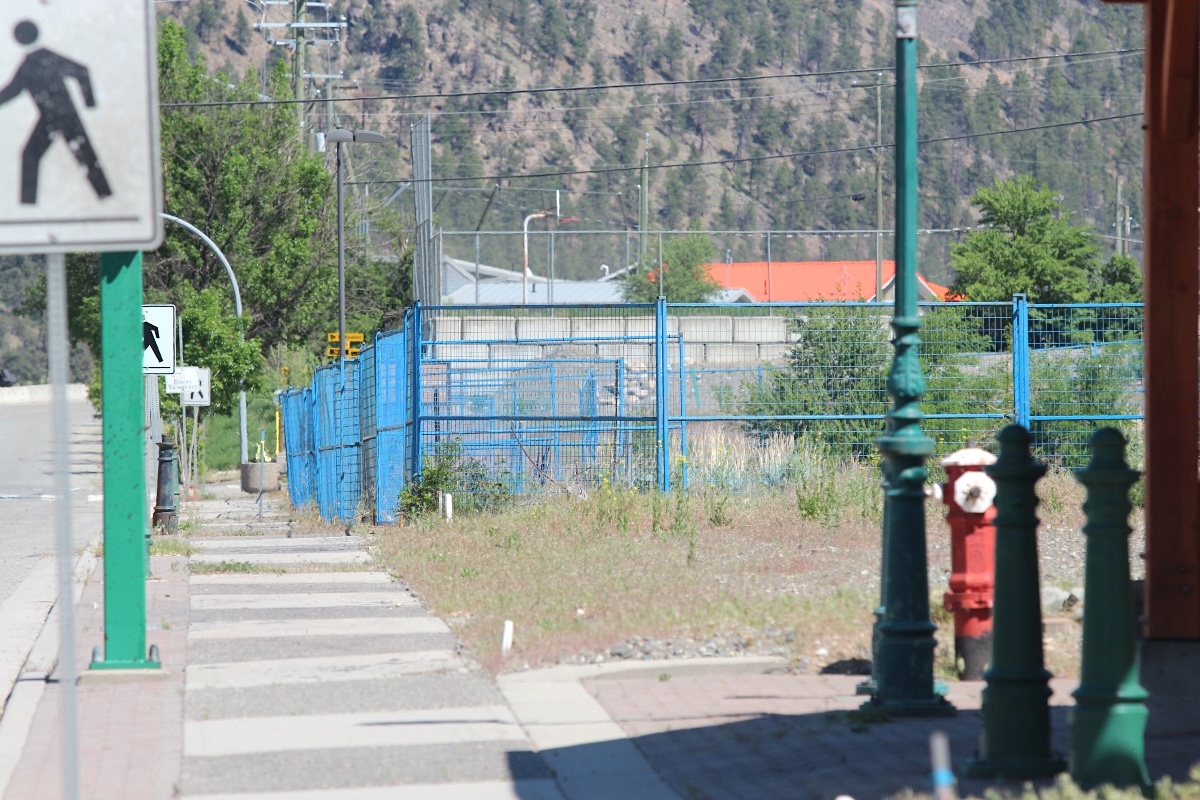 A view of a Lytton sidewalk with blue construction fencing and mountains behind.