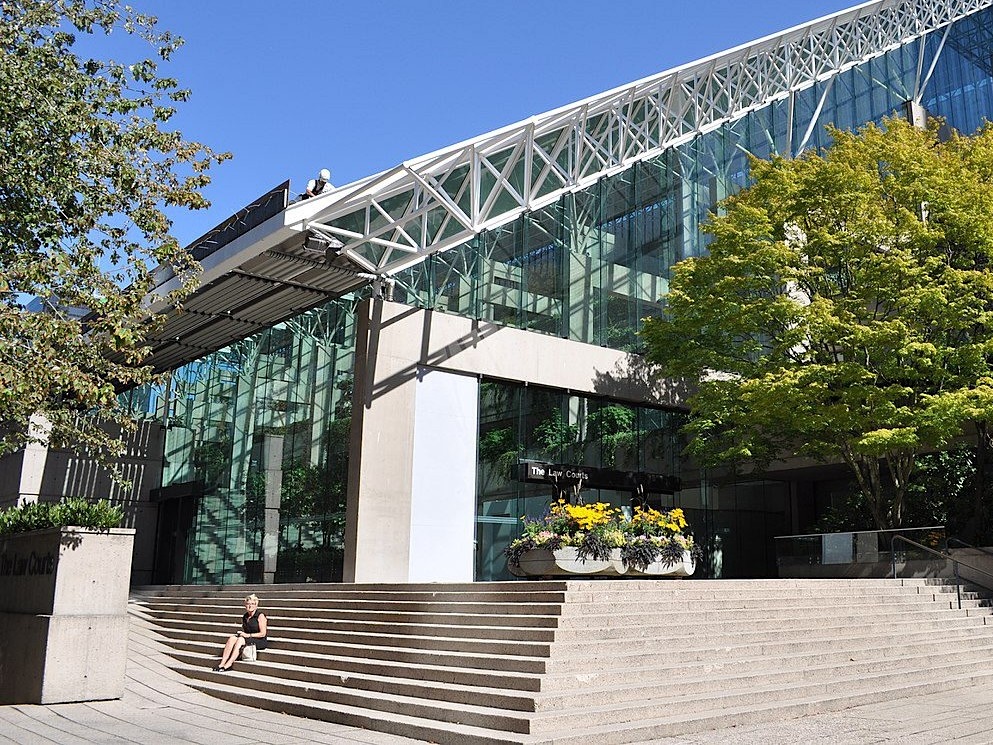 The slanted glass-roofed Vancouver Law Courts, with a person sitting on its steps.