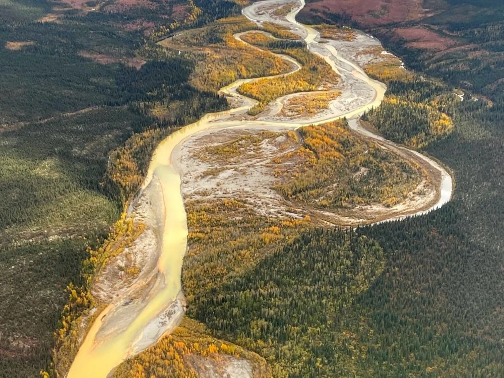 An aerial photo of a yellow-coloured river meandering through a valley.