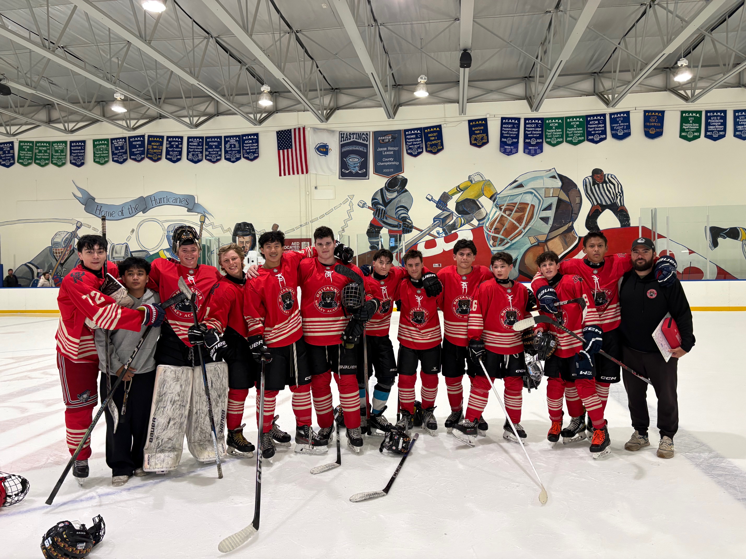 About 20 players in red hockey uniforms pose with their coach in an arena.