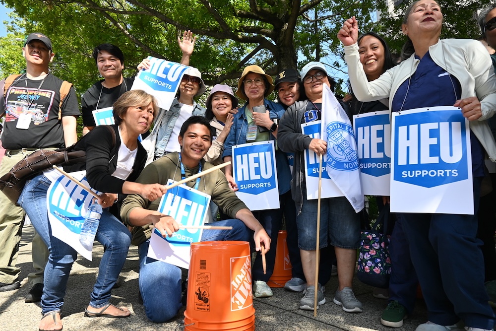 Members of the Hospital Employees Union wear blue and white signs of support and use 5-gallon Home Depot buckets to drum in support of the Nurses&rsquo; union.