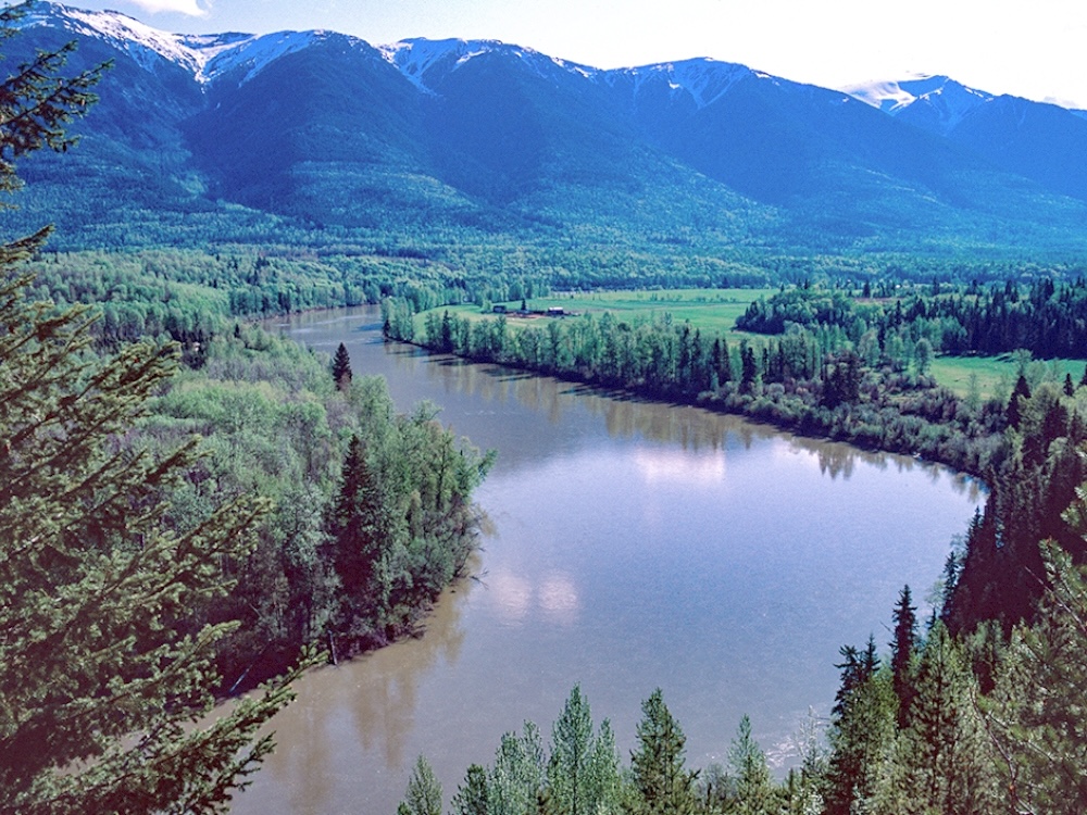 A large river runs through a scenic valley full of trees and scattered agricultural parcels