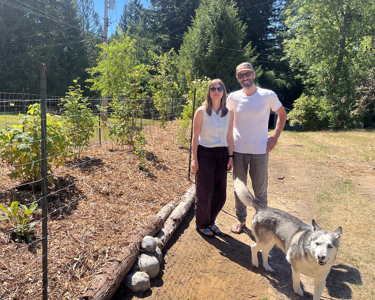 A man and woman with light skin tone both wear sunglasses. Klassen has long brown hair; Kearney is wearing a baseball cap. There is a dog, who looks like a husky, in the foreground. 