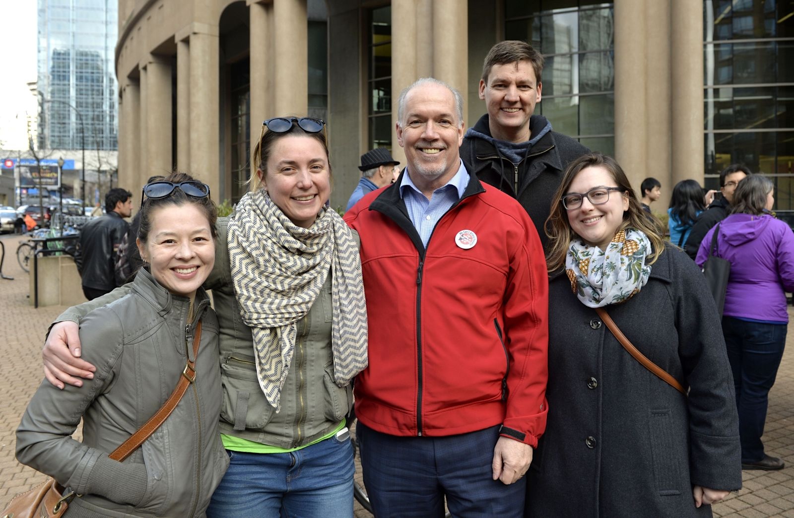 David Eby, John Horgan and three other people pose for a group photo on a city sidewalk.