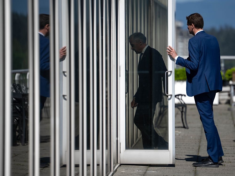 Prime Minister Mark Carney walks through a glass-paned door with Premier David Eby behind him.