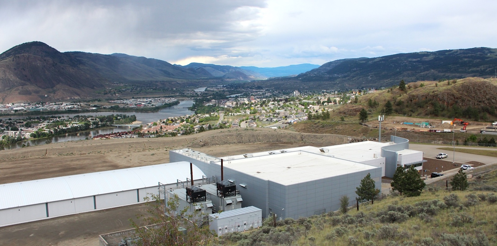 A warehouse-like building sits on a hillside overlooking a medium-sized city in an arid river valley.