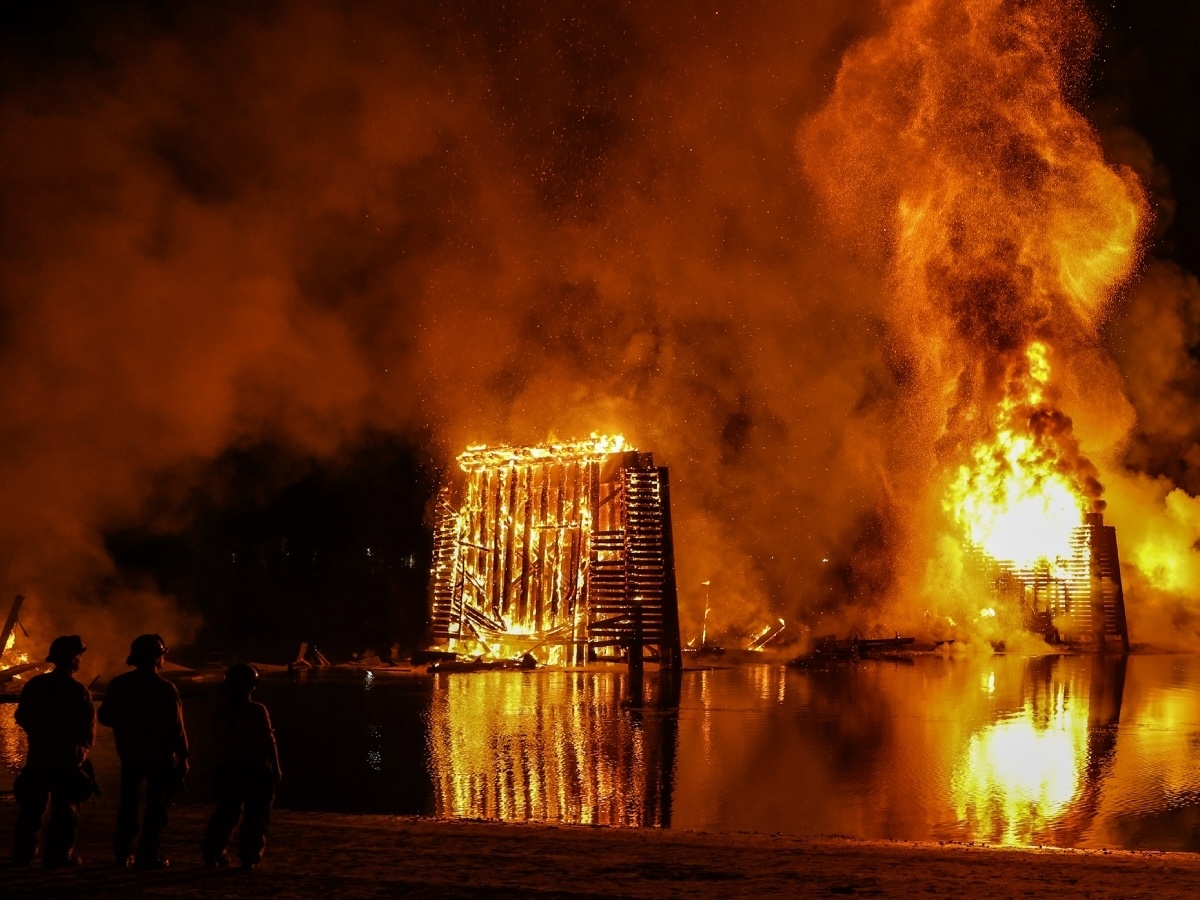 A wooden bridge is engulfed in flames at night.