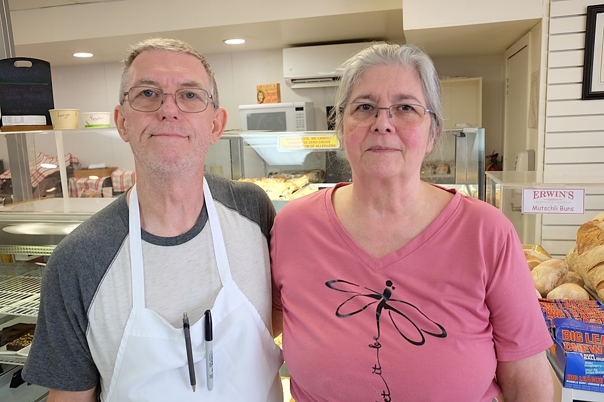 A man and a woman stand in the front of a small bakery.