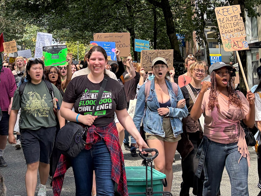 A group of people hold signs opposing an AI data centre as they march down a street in Vancouver.