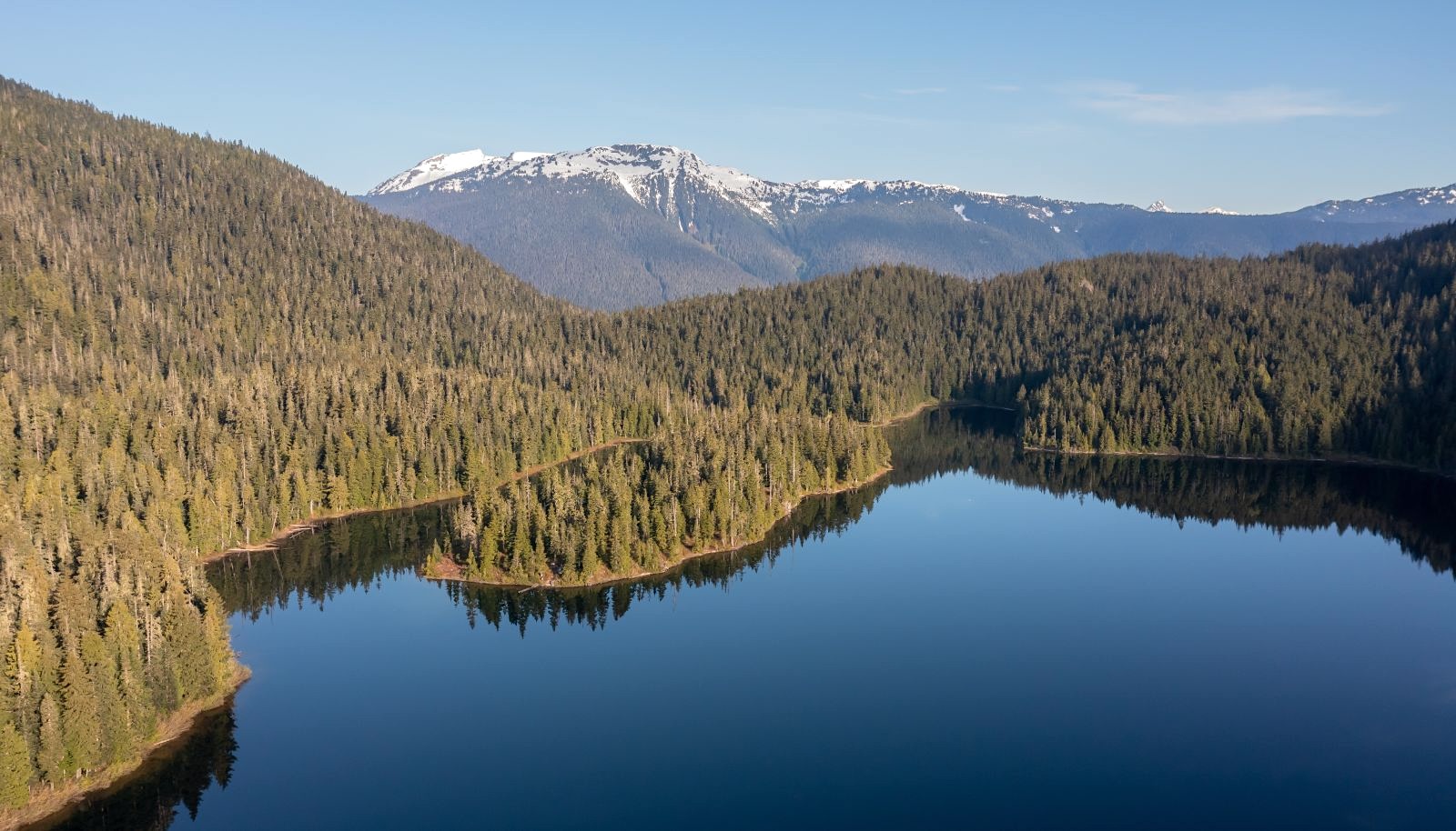 A lake surrounded by forested hills, with snow-capped mountains in the background.