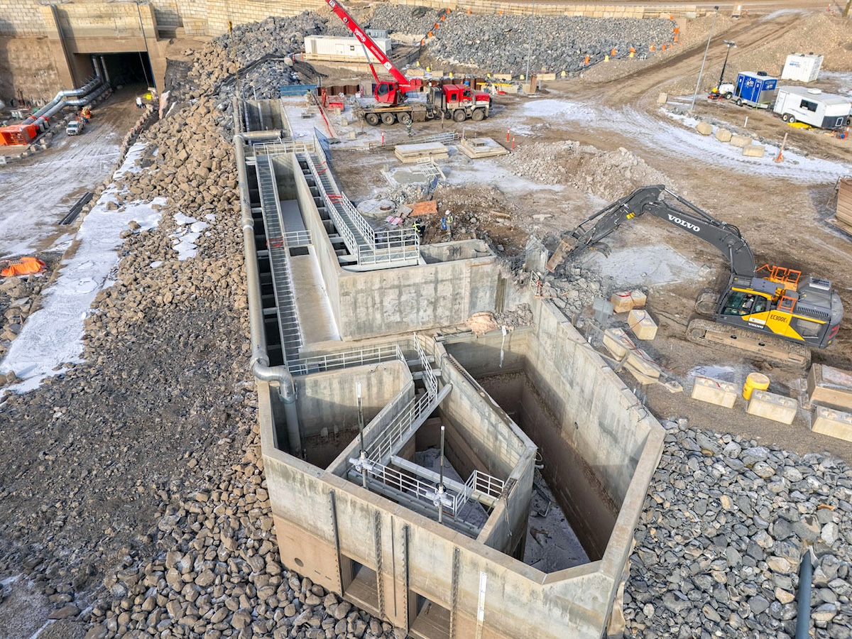 A large concrete structure rests on stones, with construction equipment working beside it.
