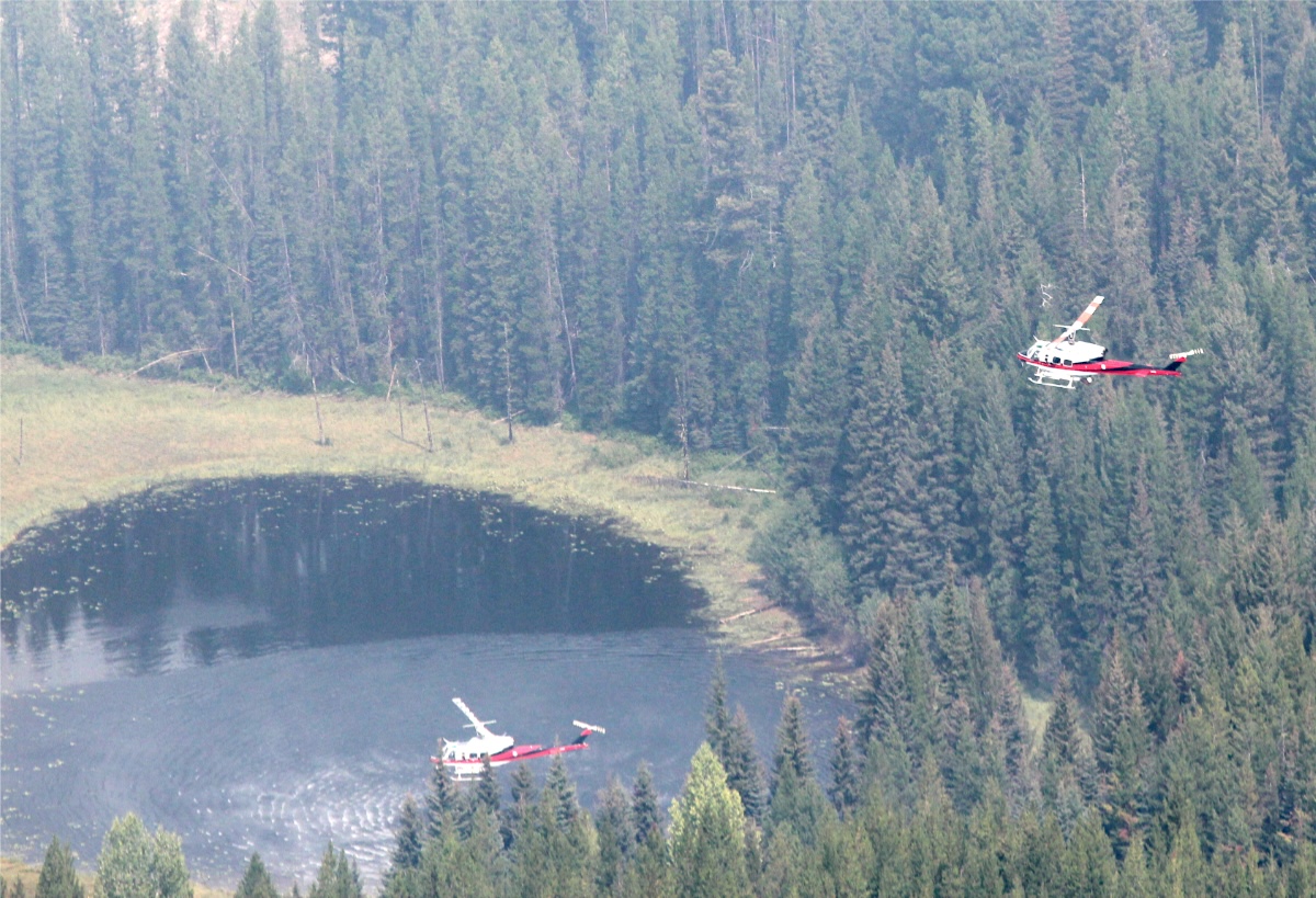 A helicopter hovers above a pond while another holds its place above. 